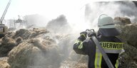 Ein Feuerwehrmann löscht einen Schwelbrand in Strohballen